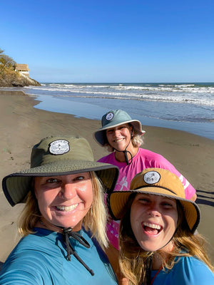 Three people wearing hats on a beach with ocean waves in the background