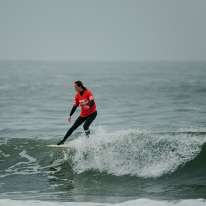 Person surfing on a wave in the ocean wearing a red rash guard during a competition. 
