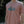 A man wearing a dusty pink t-shirt with a retro-style 'SURF SISTER' graphic in teal and white on the chest, set against a blurred outdoor background.