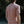A man viewed from behind wearing a dusty rose  t-shirt, standing outdoors against a dark, blurred background of trees.