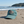 Blue cap with Surf Sister logo on a sandy beach with ocean and trees in the background