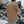 A person viewed from behind wearing a brown t-shirt and light blue jeans, standing outdoors against a rocky shoreline background.