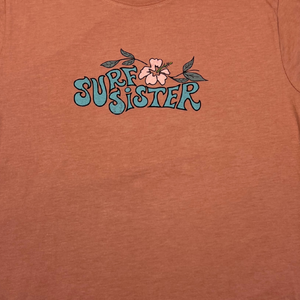 Pink t-shirt with 'Surf Sister' text and floral design on a plain background