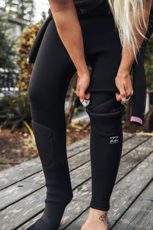 Person pulling up the knee of a wetsuit on a wooden deck
