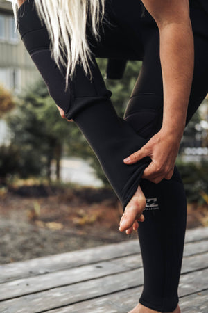 Person wearing black wetsuit with a Billabong brand logo, standing on a wooden deck.