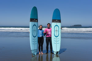 Two people standing on a beach holding two blue surfboards.
