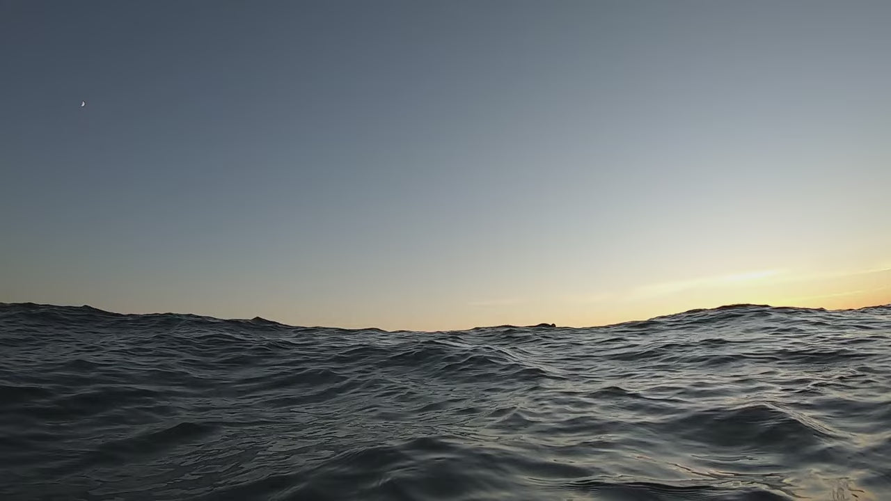 a woman surfing, surfing towards the camera on a small wave at sunset