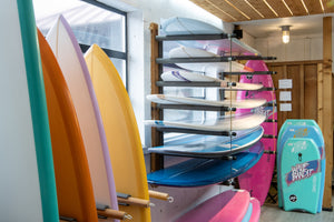 Colorful surfboards and bodyboards displayed on a rack in a store.