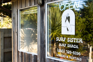 Surf Sister surf shack sign on a window with reflection of palm tree.