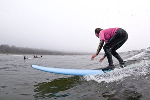 Person surfing on a blue surfboard in the ocean with a cloudy sky.