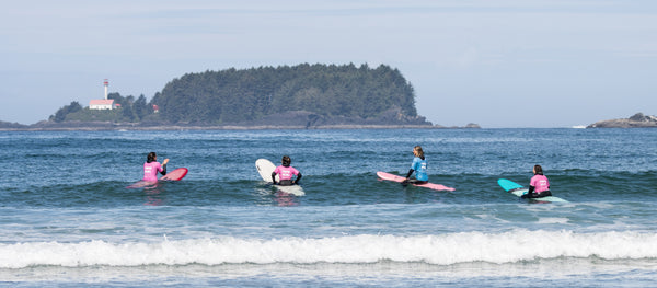 People on surfboards in the ocean with a lighthouse and island in the background.