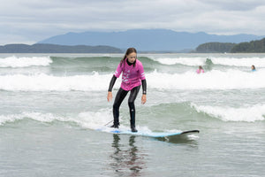 Teenage girl surfing on a small wave with mountains in the background