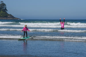 One person arms up cheering for a kid surfing in small waves 