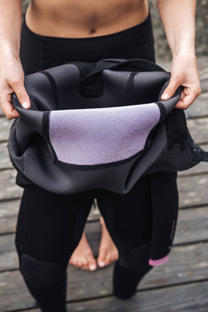 Person holding a wetsuit on a wooden floor
